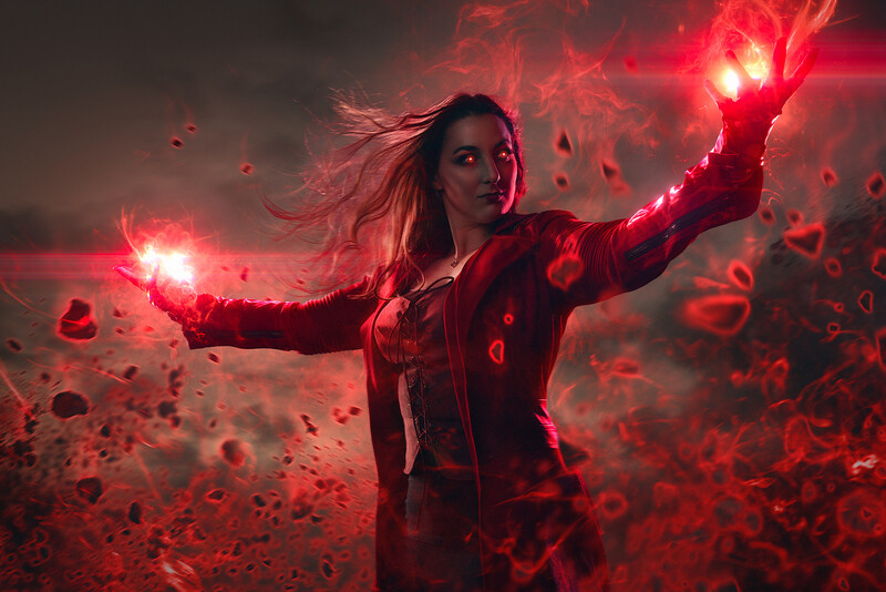 Woman with arms outstretched surrounded by glowing red magical energy and particles.