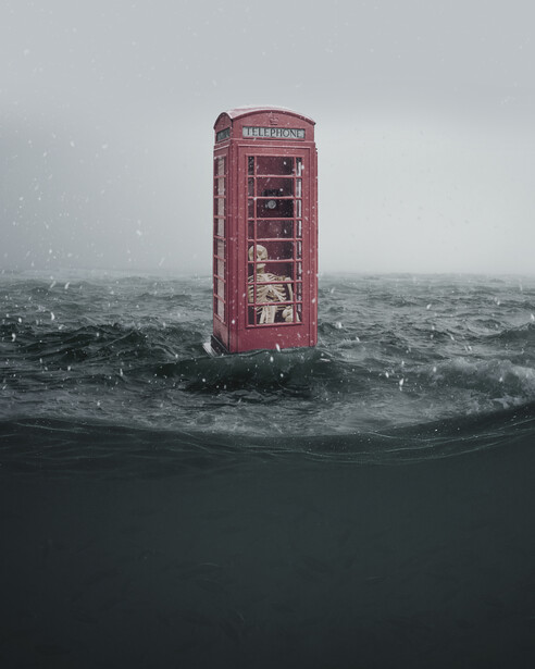 Red British telephone box half-submerged in turbulent ocean water under gray sky.