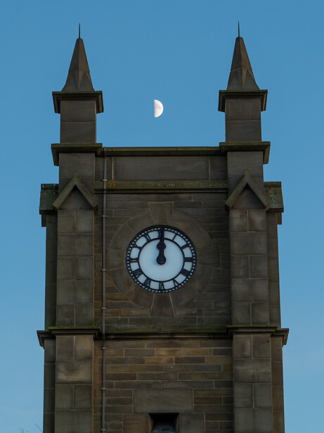 Stone clock tower with two spires against blue sky and crescent moon.