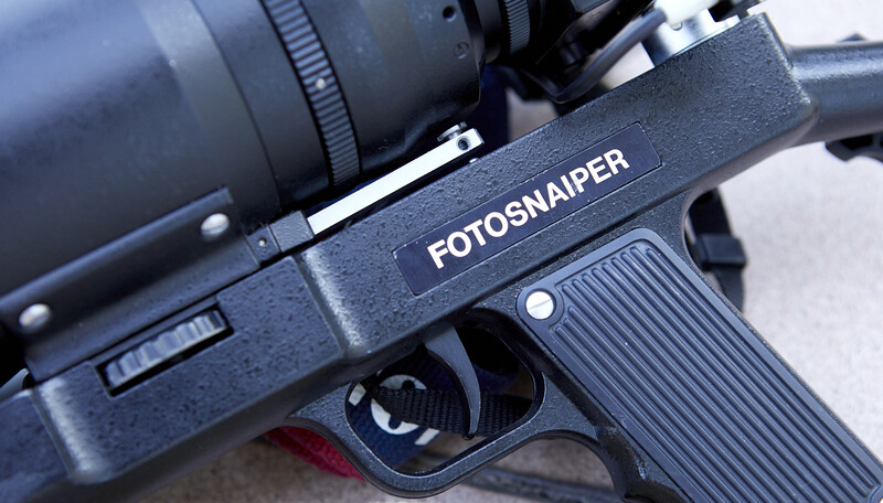 Close-up of a Fotosniper rifle-mounted camera trigger mechanism with telephoto lens attached.