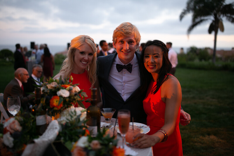 Three people posing together at an outdoor evening event with golden hour lighting and palm trees in the background.