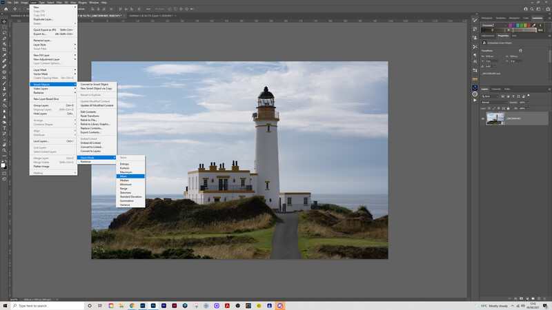 White lighthouse with attached keeper's house on a grassy headland overlooking calm sea under partly cloudy sky.