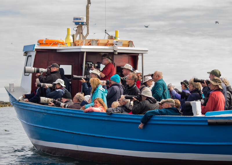 A crowded blue fishing boat filled with passengers wearing life jackets and casual clothing.