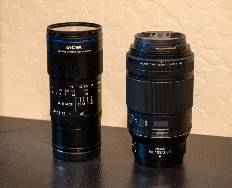 Two black telephoto lenses displayed side by side on a dark surface against a beige wall.