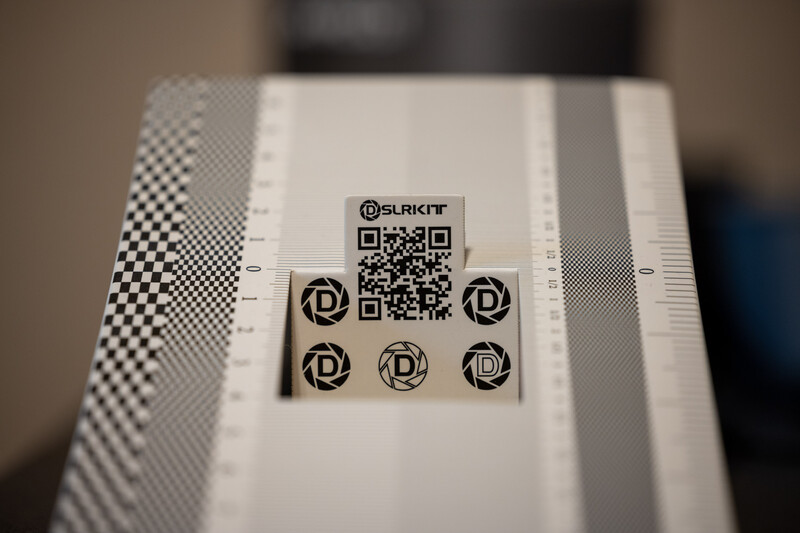 QR code and circular logo symbols printed on white material with gray striped border and checkered pattern edge.