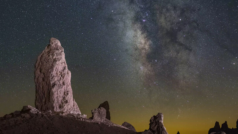 Tall rock formation illuminated against the Milky Way and starry night sky.