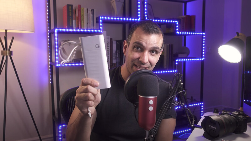 Content creator holding a tablet while speaking into a condenser microphone in a studio with purple LED lighting.