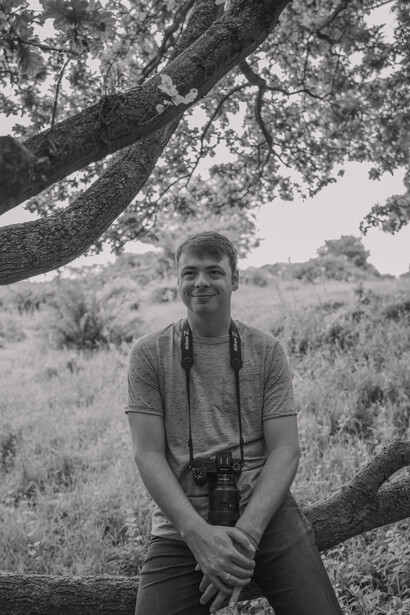 Man sitting beneath a large tree branch in an open field, looking at camera.