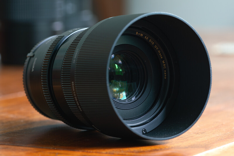 Telephoto zoom lens with lens hood attached, positioned on wooden surface with blurred background.