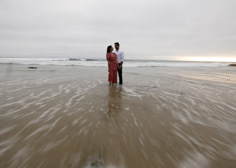 Couple wading in shallow ocean water at a beach during overcast conditions.