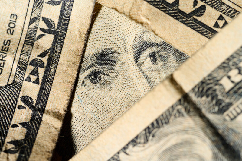 Close-up detail of layered U.S. dollar bills showing portrait and decorative border elements.