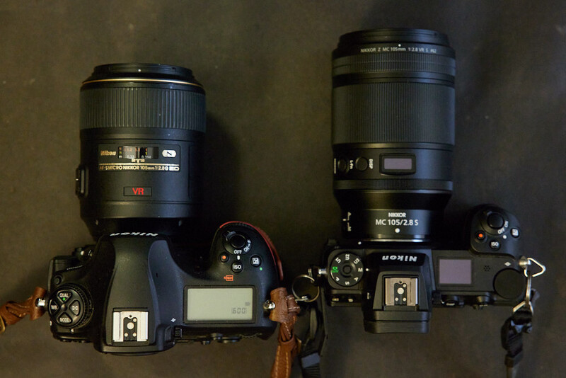 Two DSLR camera bodies with telephoto and macro lenses arranged on a neutral surface.