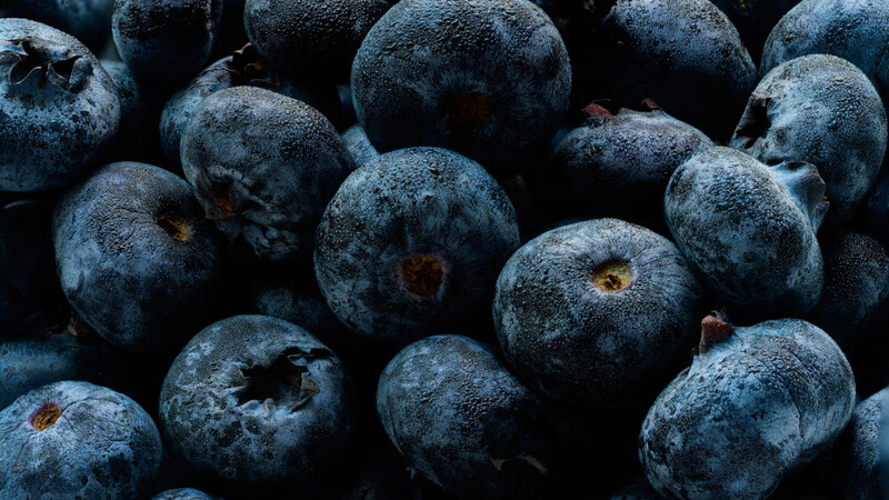 Close-up of fresh blueberries with dusty bloom coating and visible crown indentations on dark background.