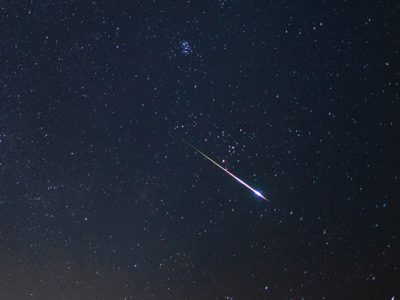 Bright meteor streaking diagonally across a dark starry night sky.