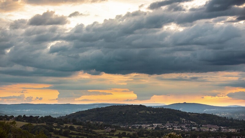 Dramatic sunset landscape with layered hills silhouetted against golden and gray clouds.