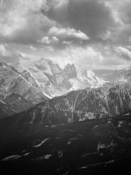 Alpine mountain landscape with forested valleys and dramatic cloudy sky.