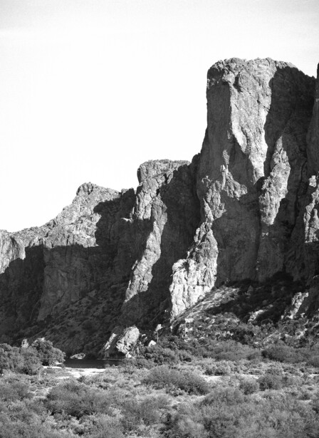 Tall columnar rock formations rising from desert scrubland under bright sunlight.