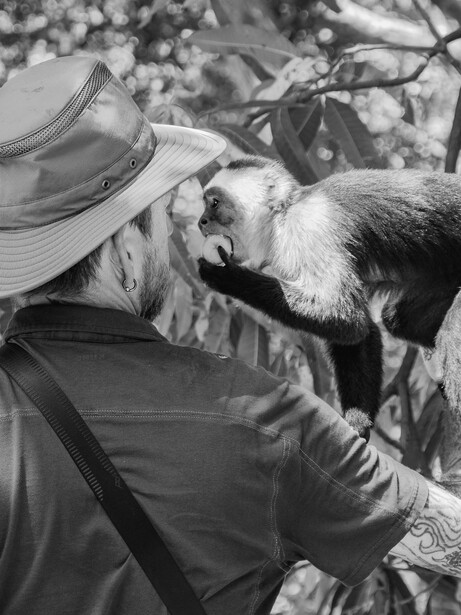 Person in cowboy hat hand-feeding a goat in black and white photography.