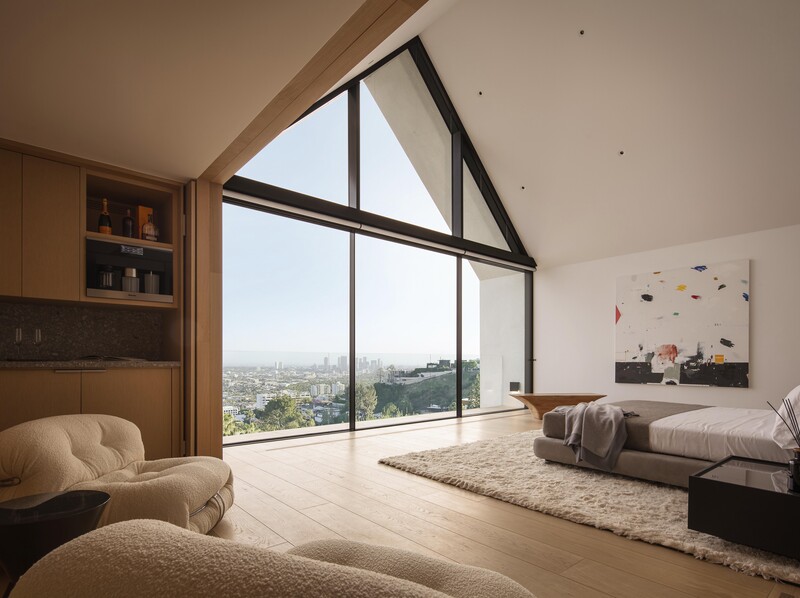Modern bedroom with floor-to-ceiling triangular windows overlooking a sprawling cityscape at daytime.