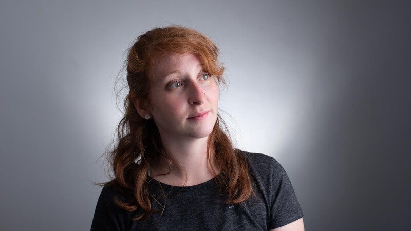 Woman with reddish-brown hair against a soft, diffused gray background looking upward.