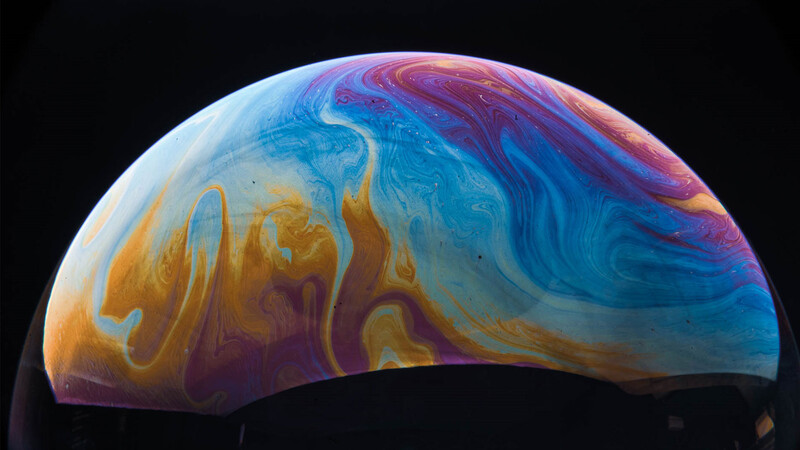 Soap bubble with swirling patterns of blue, purple, orange, and gold against black background.