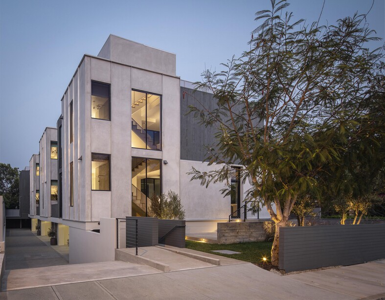 Modern residential building photographed at dusk with warm interior lighting and landscape trees.