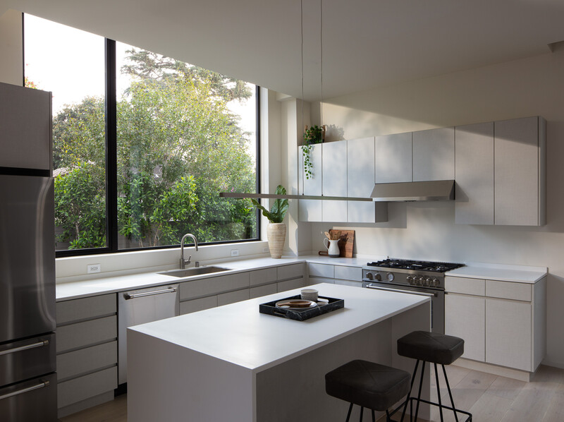 Modern kitchen with white cabinetry, island seating, and large windows overlooking green landscape.