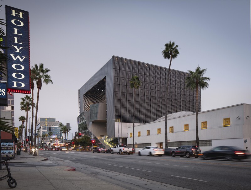 Modern architectural building with dark grid facade next to white structure on Hollywood Boulevard with palm trees.