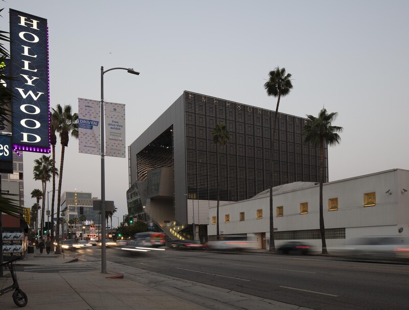 Modern architectural building with dark upper section and white lower section on a city street at dusk.