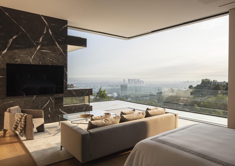 Modern bedroom with floor-to-ceiling windows overlooking a sprawling cityscape shrouded in haze.