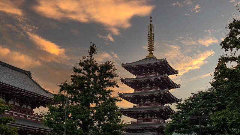 Multi-tiered pagoda with golden spire silhouetted against dramatic sunset sky with orange clouds.