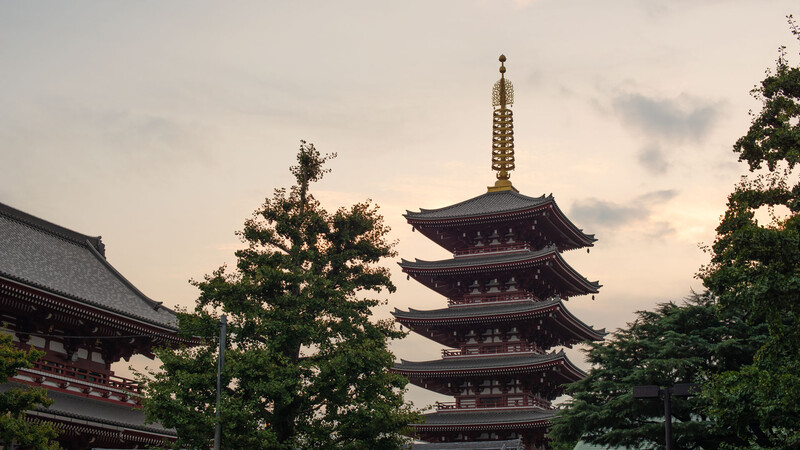 Traditional East Asian pagoda with five tiers and ornate spire surrounded by temple buildings and green foliage.