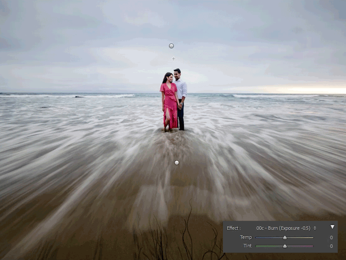 Couple standing in shallow ocean water with motion blur from incoming waves.