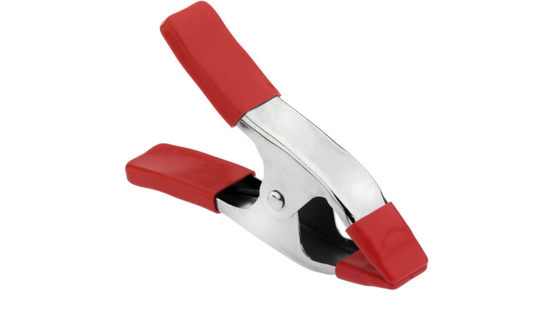 Red and silver spring clamp with padded handles and open jaws against white background.