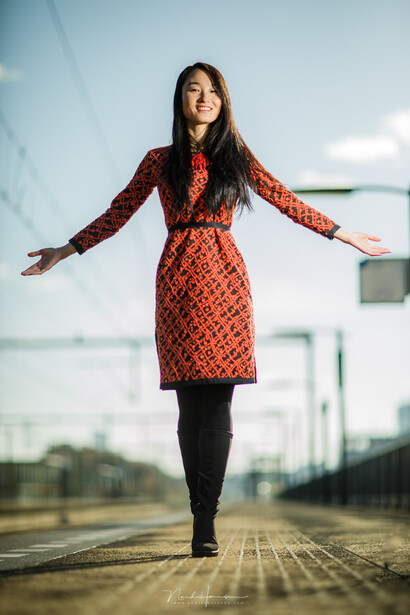 Woman in red patterned dress with arms outstretched standing on wooden boardwalk.