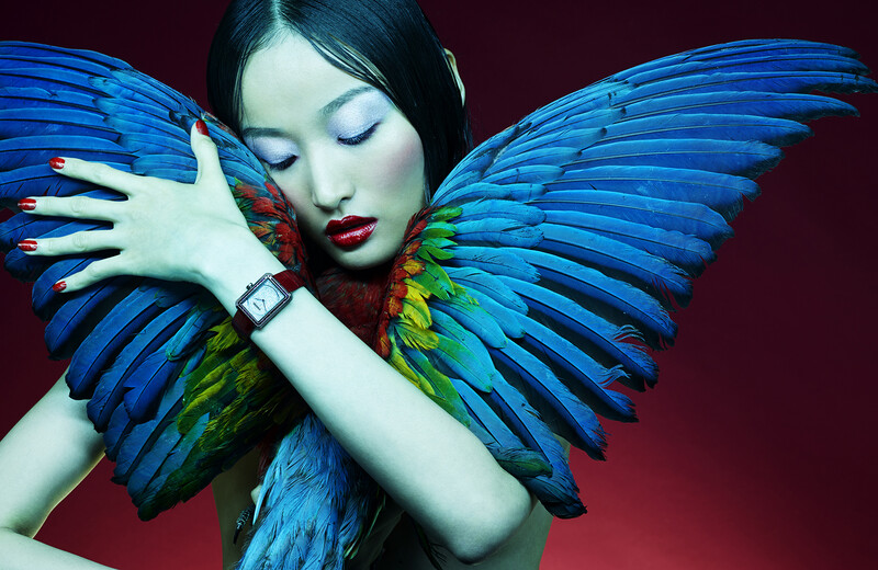 Woman with blue feathered wings and vibrant red lips against burgundy background.
