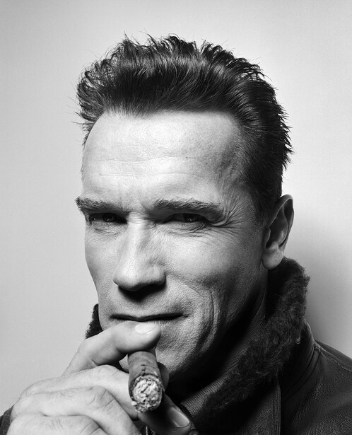 Black and white portrait of a man with slicked-back hair holding a cigar near his mouth.