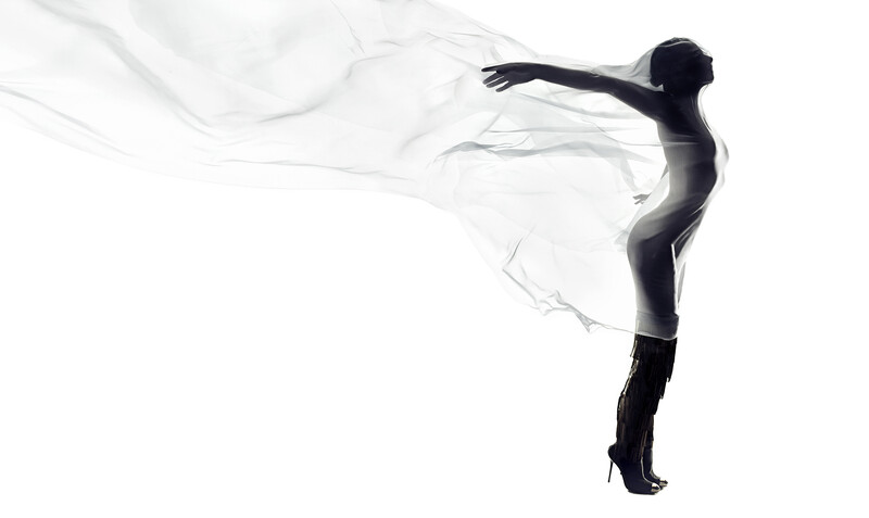 Silhouetted figure in high heels with sheer fabric flowing behind them against white background.