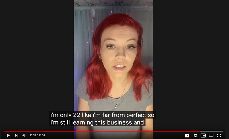 Person with bright red hair wearing a gray shirt, looking directly at camera in indoor setting.