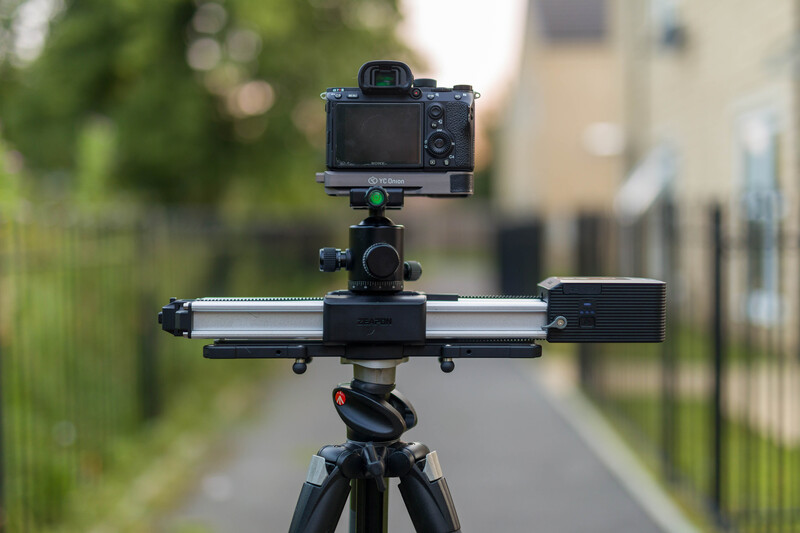 Mirrorless camera mounted on tripod with slider rail and gimbal head in outdoor residential setting.