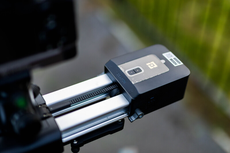 Close-up of a motorized camera slider with dual white rails mounted on a support arm.