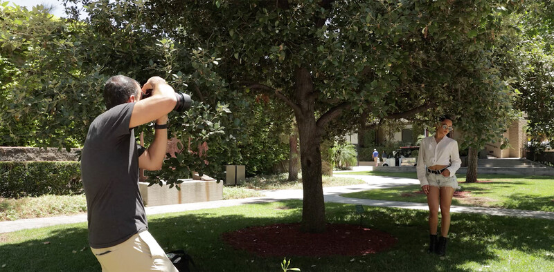 Photographer shooting a portrait of a subject in a tree-lined campus setting with natural window light.