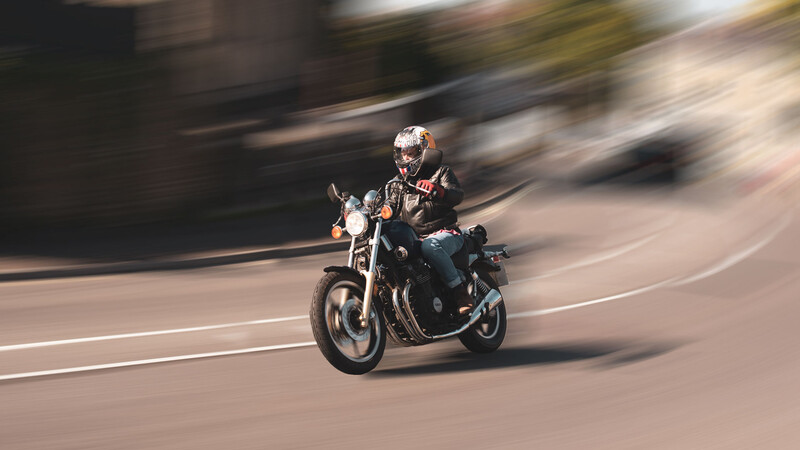 Motorcyclist riding a cruiser through a curved street with motion blur effect.