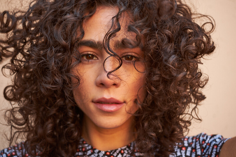 Person with voluminous curly dark hair and round glasses looking directly at camera.