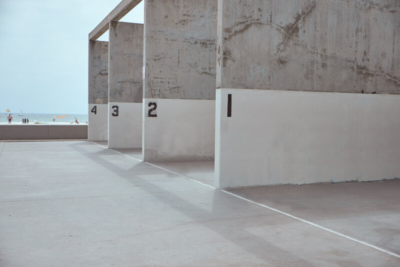 Minimalist concrete parking structure with numbered bays and stark white dividing walls under overcast sky.