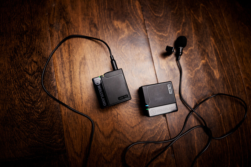 Two wireless microphone receivers and a lavalier microphone on a wooden surface.