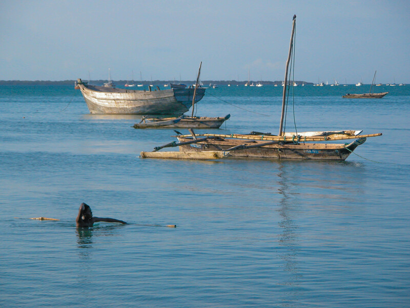 Traditional wooden fishing boats anchored in shallow turquoise water with a swimmer visible in the foreground.