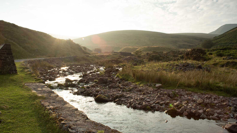 Mountain valley with meandering stream and golden-hour sunlight illuminating rolling hills.