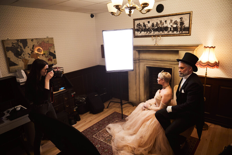 Behind-the-scenes wedding portrait session with photographer, bride, and groom in formal studio setting.