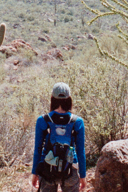 Hiker with blue backpack walking away from camera on dry, sparse hillside terrain.